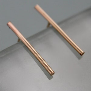 May include: A pair of rose gold bar earrings. The earrings are simple and minimalist, with a straight bar design.