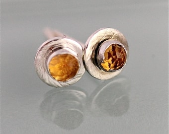 May include: A pair of silver earrings with small round orange gemstones set in the center of each earring.