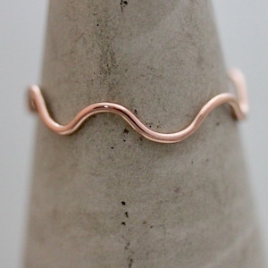 May include: A delicate rose gold ring with a wavy design. The ring is made of thin wire and has a simple, elegant look.