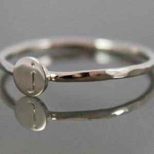 May include: A silver ring with a hammered band and a round disc featuring the letter "J" in the center.