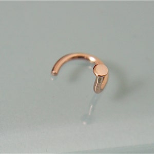 May include: A small, gold-toned nose ring with a round, flat top.