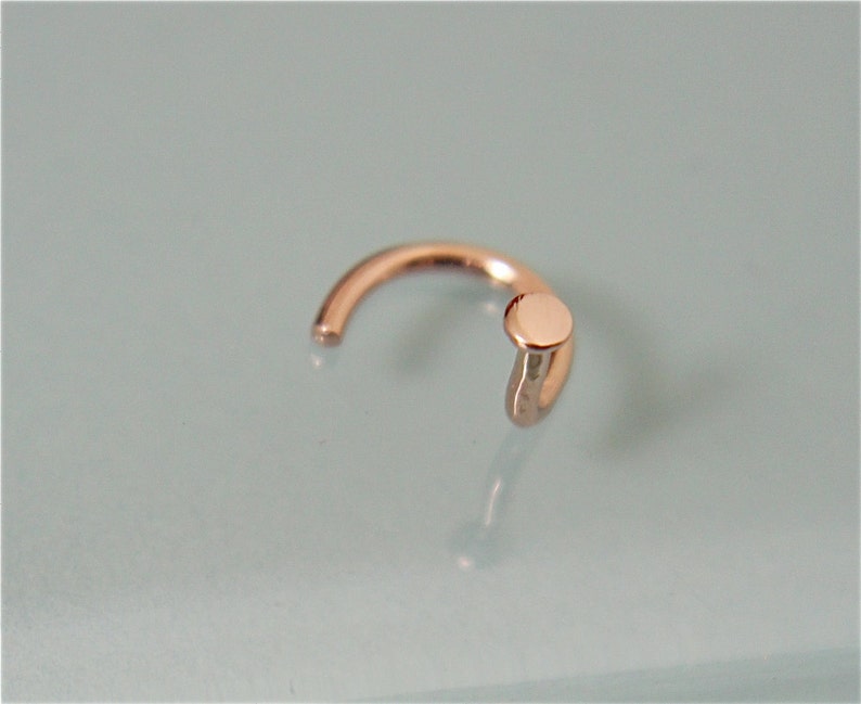 May include: A small, gold-toned nose ring with a round, flat top.