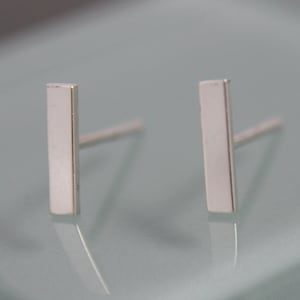 May include: A pair of silver bar stud earrings. The earrings are simple and minimalist, with a rectangular shape.