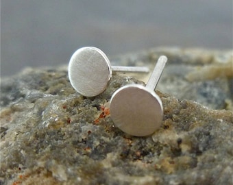 May include: A pair of silver stud earrings with round, flat, brushed metal fronts.