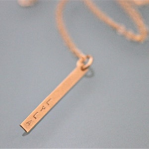 May include: A gold necklace with a thin, rectangular pendant that has the word "LYLA" engraved on it.