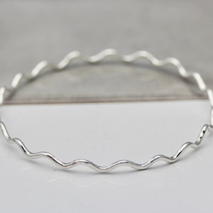 May include: A silver bangle bracelet with a wavy design.