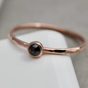 May include: A delicate rose gold band ring with a black diamond set in a bezel setting.
