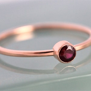 Op de afbeelding: Een delicate ring van ros&eacute;goud met een enkele, ronde, dieprode edelsteen in een bezel-setting.