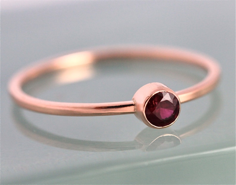 Op de afbeelding: Een delicate ring van ros&eacute;goud met een enkele, ronde, dieprode edelsteen in een bezel-setting.