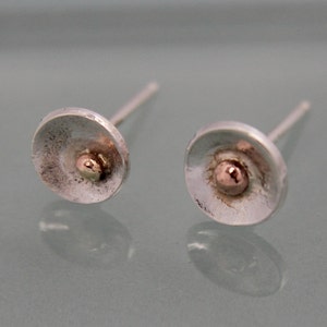 May include: A pair of silver stud earrings with a small rose gold dot in the center of each earring.
