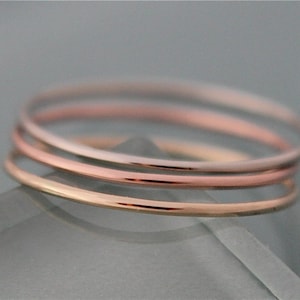 May include: Three thin gold rings stacked on top of each other. The top ring is white gold, the middle ring is rose gold, and the bottom ring is yellow gold.