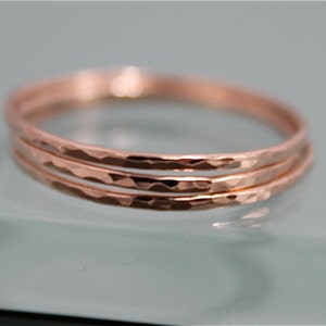 May include: Three thin rose gold rings stacked together. The rings have a hammered texture.