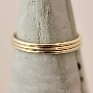 May include: Three gold rings stacked on top of each other. The rings are simple and delicate, with a smooth, polished finish.