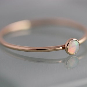 May include: A delicate rose gold ring with a small, round, white opal gemstone.