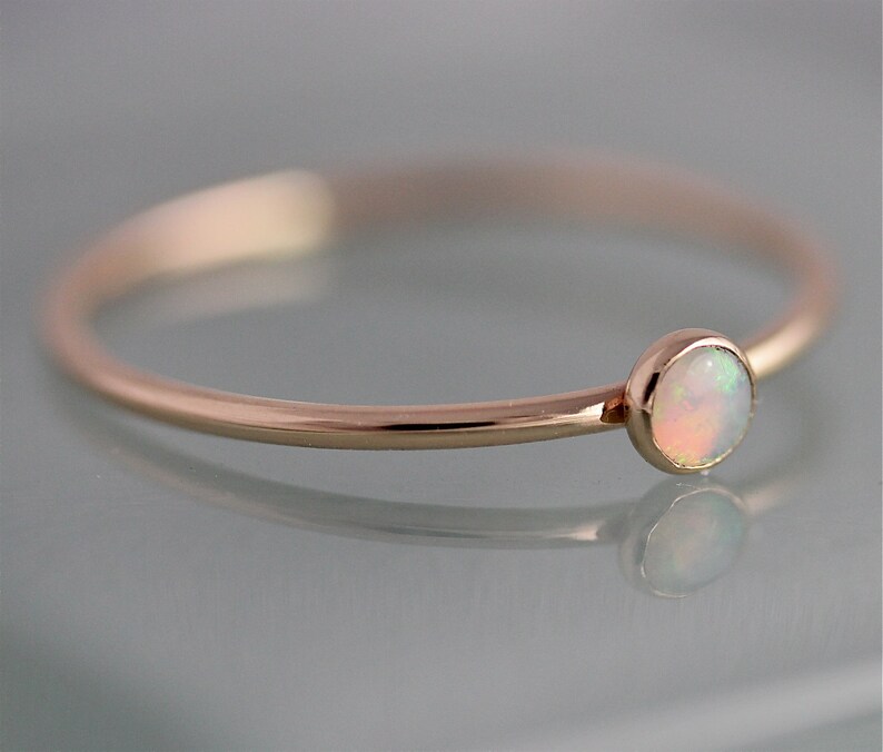 May include: A delicate rose gold ring with a small, round, white opal gemstone.