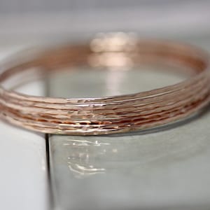 May include: A set of five rose gold hammered bangle bracelets. The bracelets are stacked on top of each other, creating a layered look.