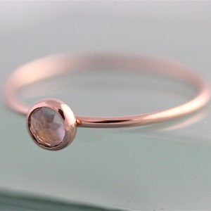 May include: A delicate rose gold ring with a single, clear gemstone set in the center.