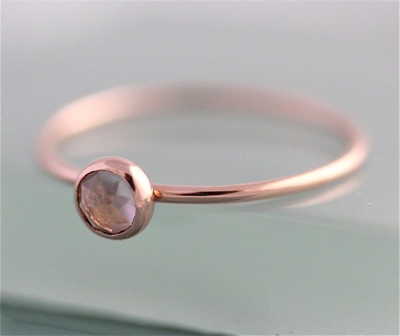 May include: A delicate rose gold ring with a single, clear gemstone set in the center.