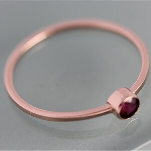 Op de afbeelding: Een delicate ring van ros&eacute;goud met een kleine, ronde, donkerrode edelsteen.