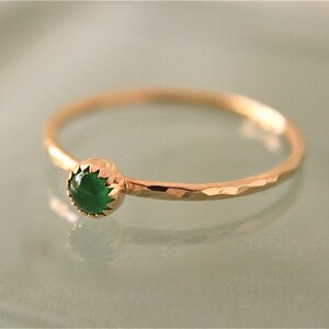 May include: A delicate gold ring with a hammered band and a bezel-set, round, emerald-green gemstone. The ring's band has a textured, faceted appearance, and the gemstone is the focal point.