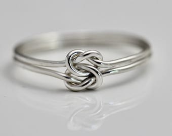 May include: A silver ring with a knot design. The ring is made of two bands of metal that are intertwined to create a knot.