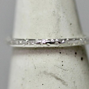 May include: A silver ring with a textured surface. The ring is thin and has a hammered finish.