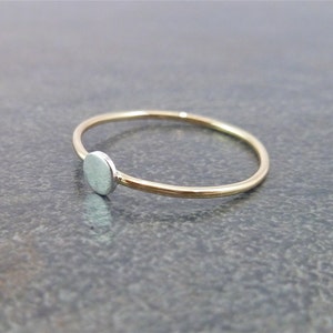 May include: A simple gold band ring with a small, round silver disc on the side.