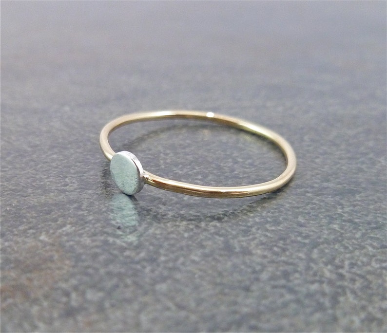 May include: A simple gold band ring with a small, round silver disc on the side.