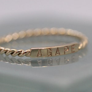May include: A gold ring with a twisted band and a rectangular plaque engraved with the word "AGAPE".