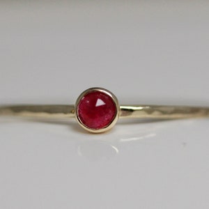May include: A delicate gold ring with a small, round, red gemstone set in the center.