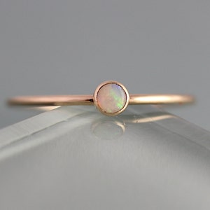 May include: A delicate rose gold ring with a single round opal gemstone.