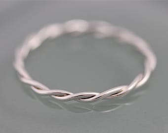 Puede incluir: Un anillo plateado con un diseño de cuerda trenzada. El anillo está hecho de un metal brillante y reflectante, con una superficie lisa. Una pieza de joyería sencilla y elegante.
