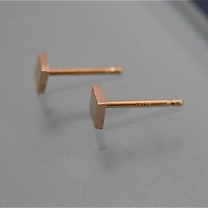 May include: A pair of gold square stud earrings. The earrings are simple and minimalist in design.