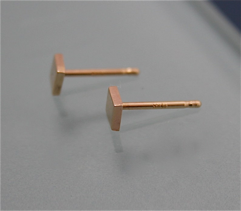 May include: A pair of gold square stud earrings. The earrings are simple and minimalist in design.