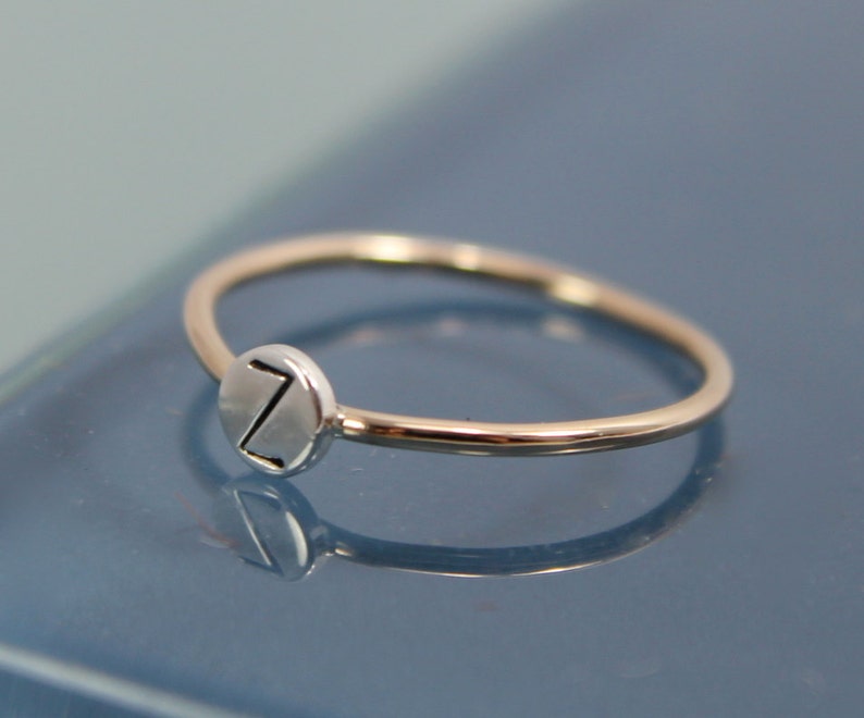 May include: A silver ring with a round, silver charm featuring the letter "Z" engraved on it.