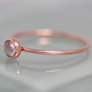 May include: A delicate rose gold ring with a single, round, iridescent gemstone set in the band.