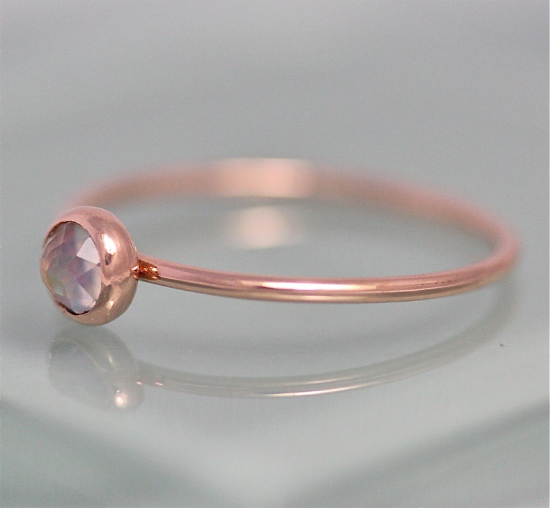 May include: A delicate rose gold ring with a single, round, iridescent gemstone set in the band.