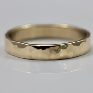 May include: A gold hammered band ring. The ring is a simple band with a hammered texture.