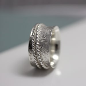 May include: A silver ring with a textured band and a beaded design. The ring is wide and has a rounded shape.