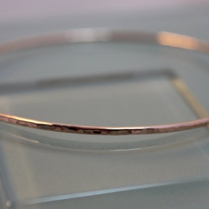 May include: A hammered rose gold bangle bracelet. The bracelet is thin and delicate, with a smooth, polished finish.