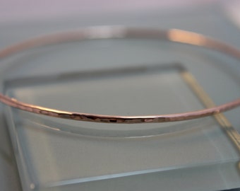 May include: A hammered rose gold bangle bracelet. The bracelet is thin and delicate, with a smooth, polished finish.