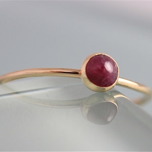 May include: A delicate gold ring with a single, round, cabochon-cut ruby gemstone.