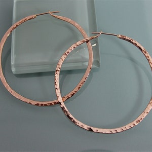 May include: A pair of large, hammered rose gold hoop earrings. The earrings are made of a thick, textured metal and have a simple, elegant design.