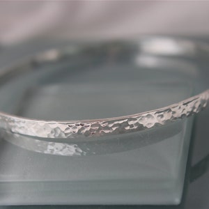 May include: A silver hammered bangle bracelet. The bracelet is smooth and shiny, with a hammered texture.