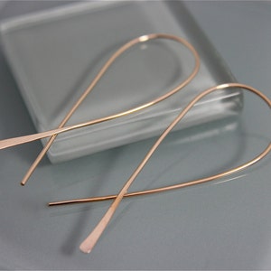 May include: A pair of rose gold hoop earrings with a simple, minimalist design. The earrings are made of thin wire and have a delicate, curved shape.