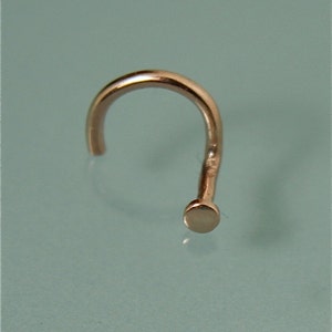 May include: A rose gold nose ring with a small, round bead at the end.