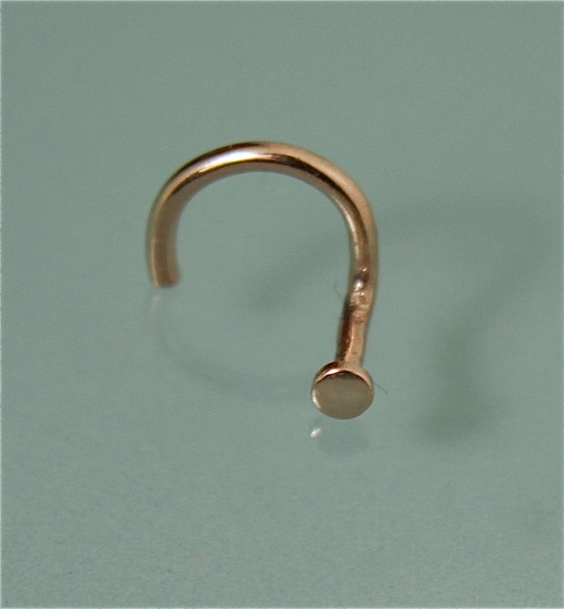 May include: A rose gold nose ring with a small, round bead at the end.