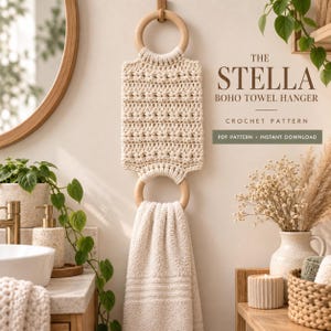 Peut inclure: Un porte-serviette en crochet couleur crème avec deux anneaux en bois clair et un motif texturé. Le texte indique : THE STELLA BOHO TOWEL HANGER CROCHET PATTERN PDF PATTERN INSTANT DOWNLOAD. Une serviette beige est suspendue à l'anneau inférieur.