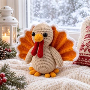 May include: A crochet turkey toy featuring a beige body, a bright orange fan-shaped tail with white scalloped edges, a yellow beak, and two red wattles. The turkey has round black eyes and small orange feet, crafted with visible yarn stitches.