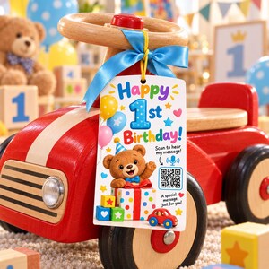 May include: A rectangular white gift tag tied with a blue ribbon to a red wooden toy car. The tag features the text Happy 1st Birthday, a cartoon bear with a party hat, colorful balloons, small blocks, a QR code, and the text Scan to hear my message.